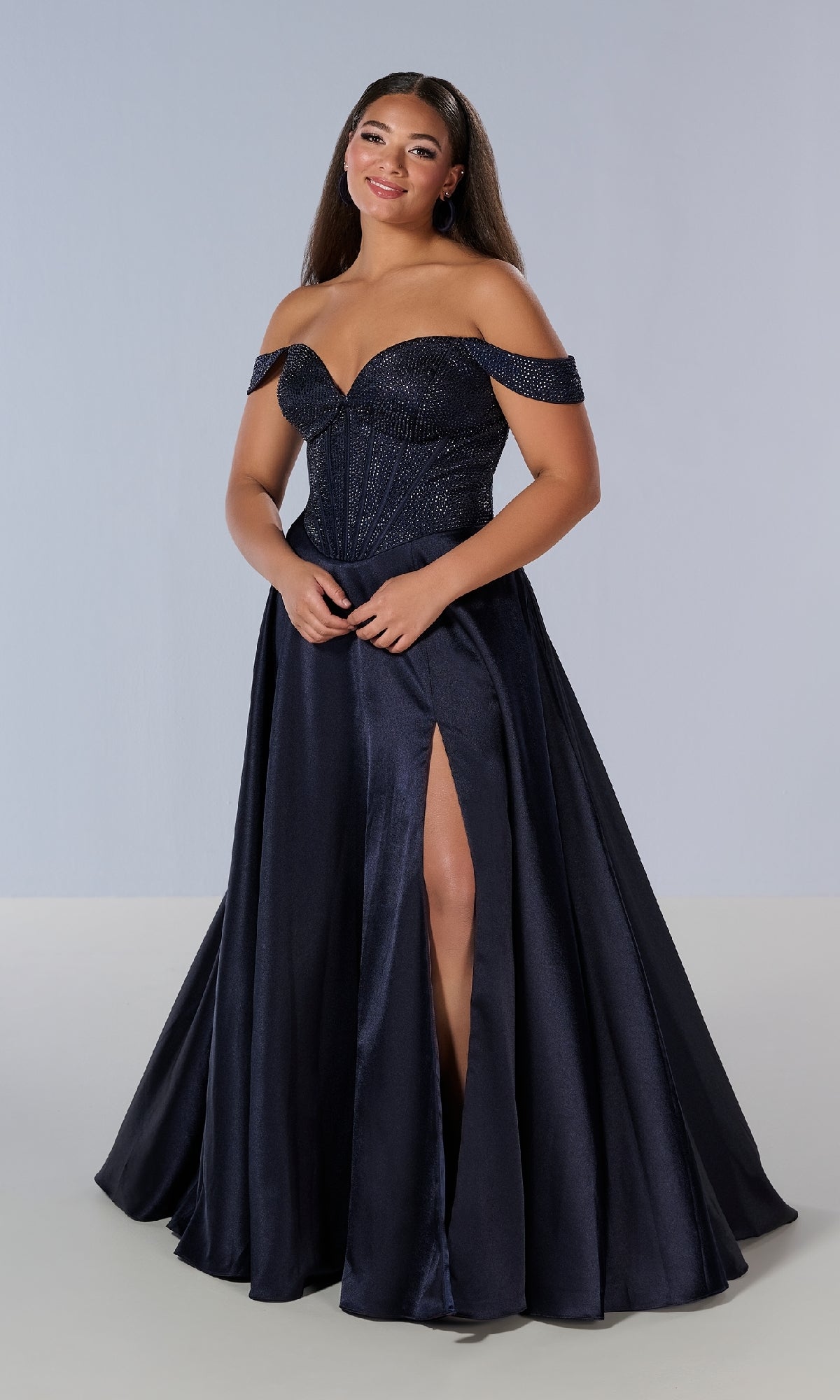 A woman poses in the Tiffany 16204 long plus-size prom dress, featuring an elegant navy off-the-shoulder design with a fitted bodice, sweetheart neckline, and high slit, standing out against a simple light background.